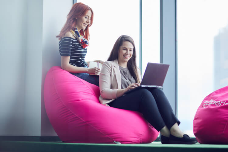 dos mujeres sentadas sonriendo mirando computador